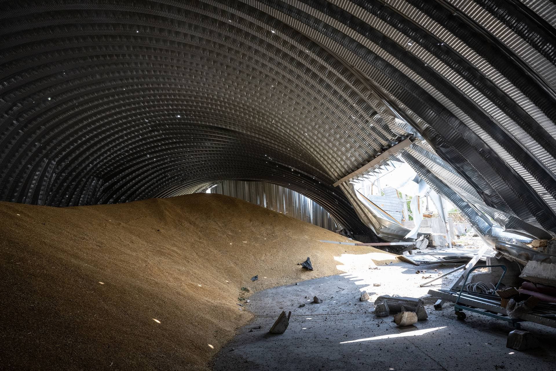 Sunlight streams through shrapnel holes onto piles of barley in Pavlivka