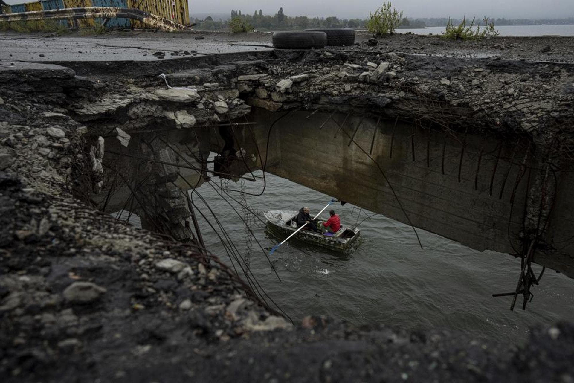 People ride on a boat across the Siverskyi-Donets river in front of a destroyed bridge in Staryi-Saltiv