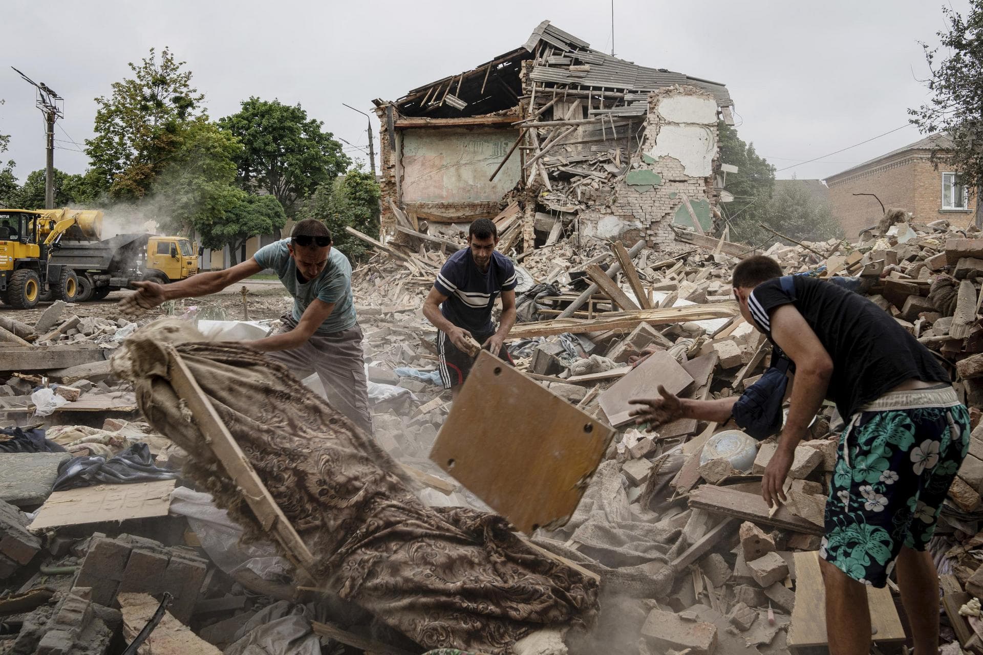 Local residents search for the documents of their injured friend in the debris of a destroyed apartment house after Russian shelling in a residential area in Chuhuiv