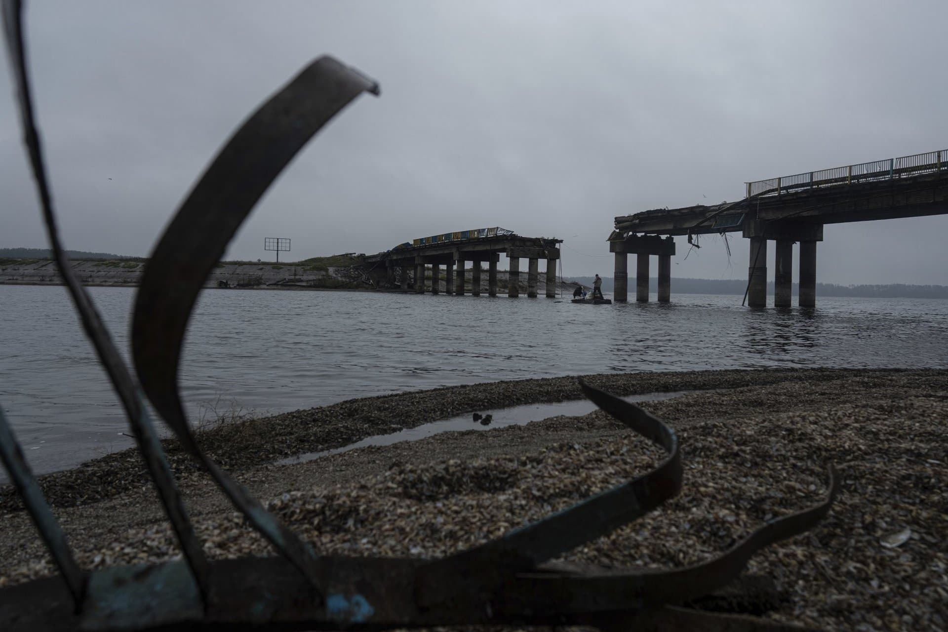 Men on a boat transport humanitarian aid across the Siverskyi-Donets river in front of a destroyed bridge in Staryi-Saltiv