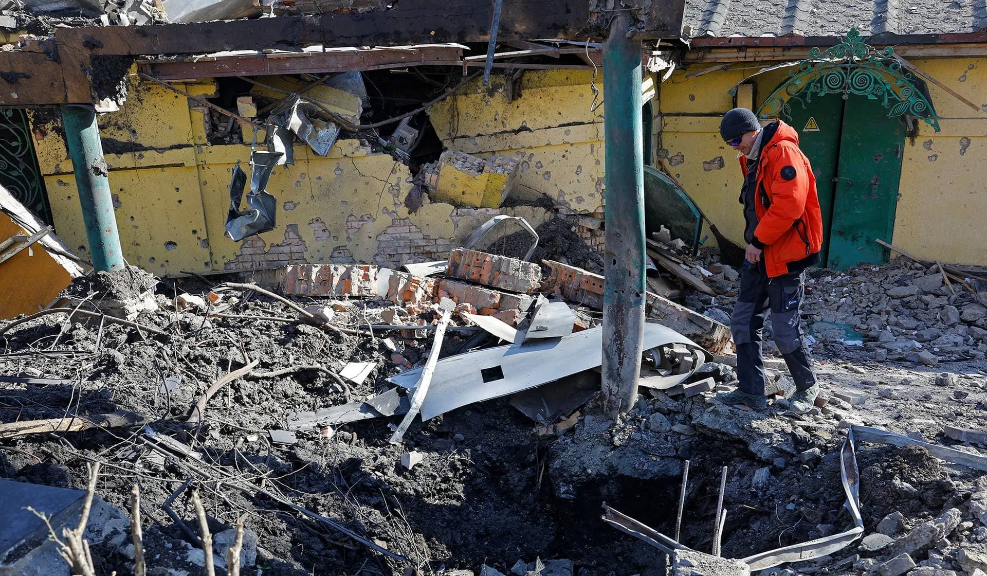 A man looks at a crater formed by recent shelling near a restaurant building in Donetsk