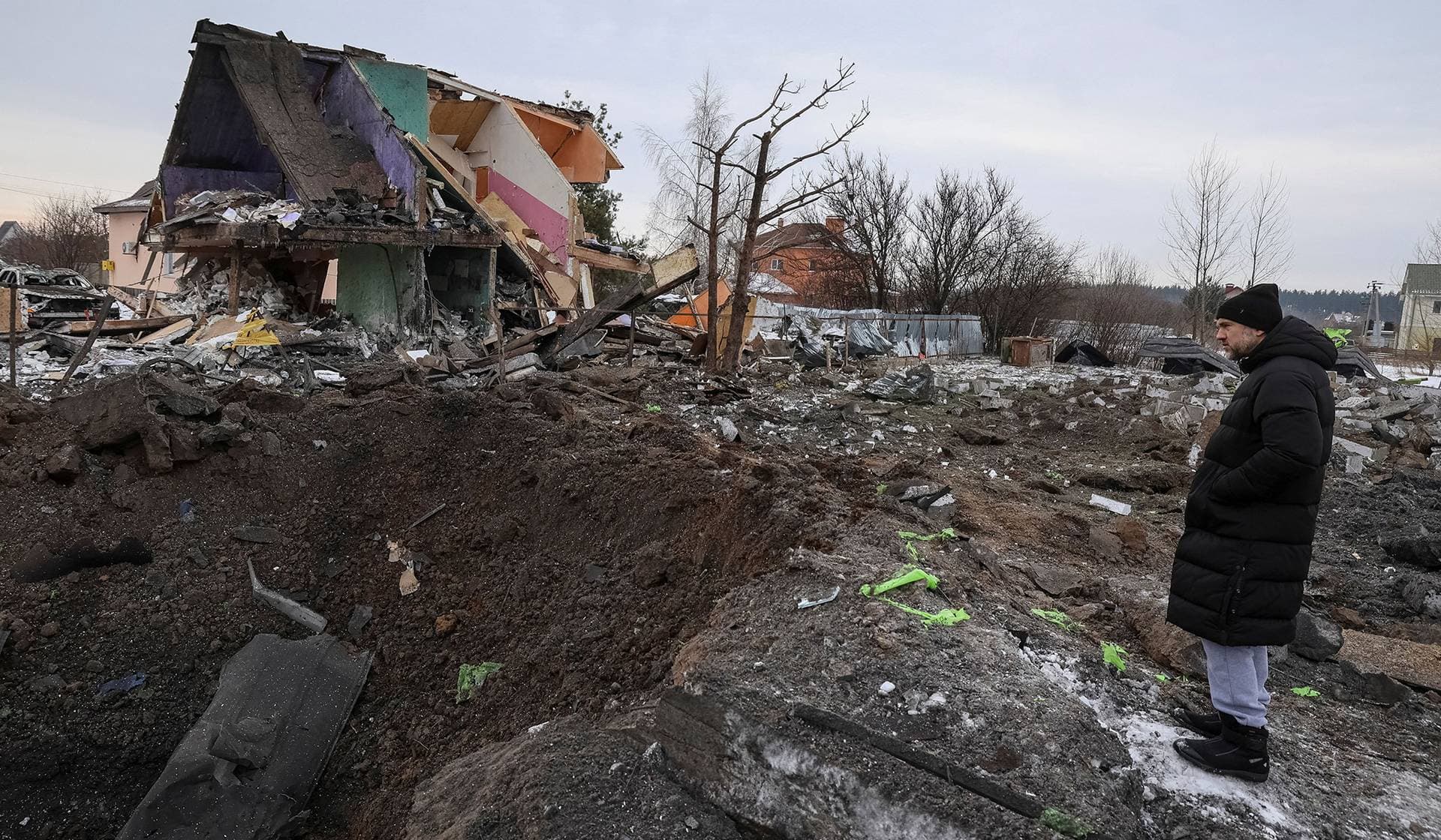 A resident stands next to a crater that appeared in front of a house during overnight Russian missile and drone strikes in the village of Putrivka