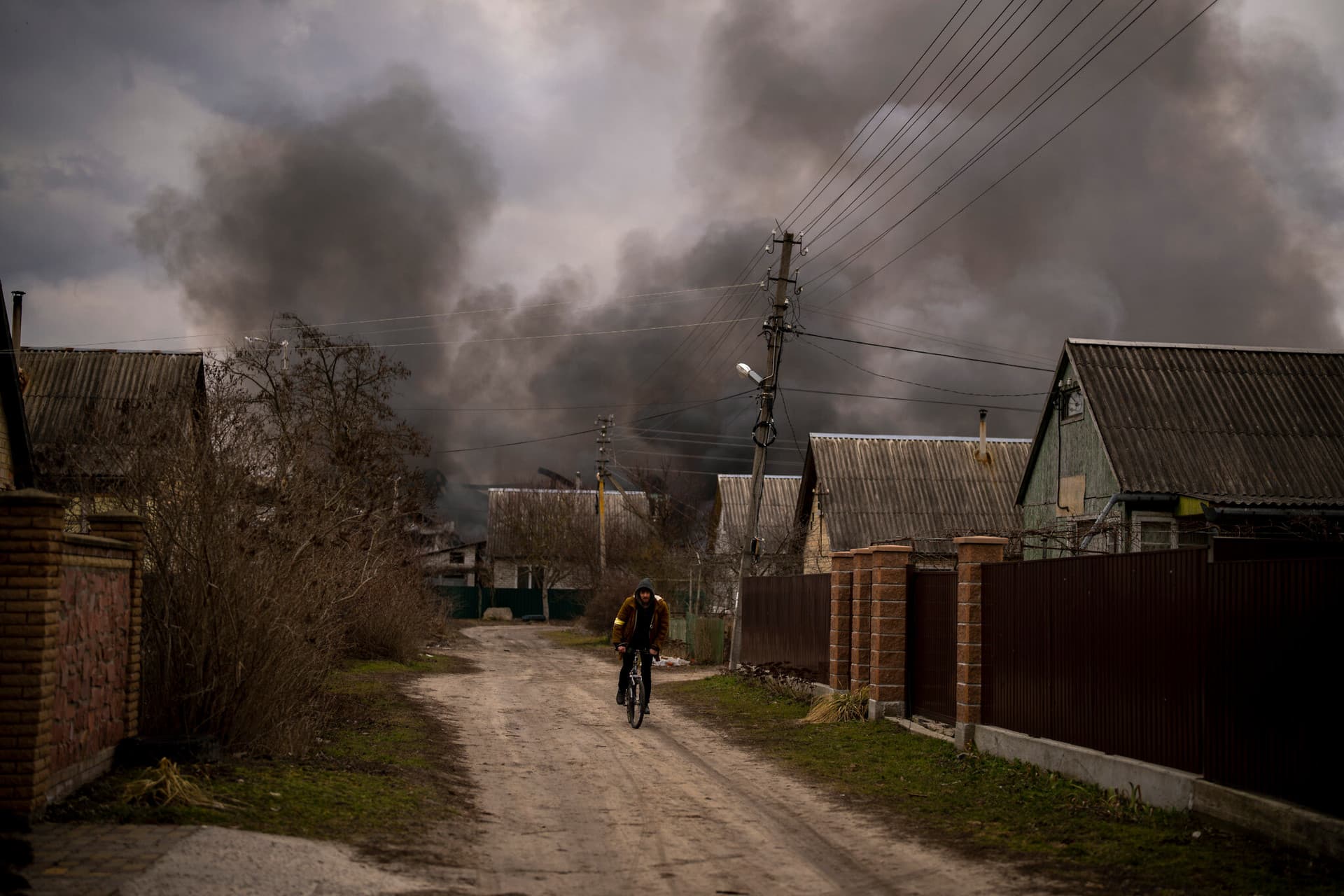 A Ukrainian man rides his bicycle near a factory and a store burning after it had been bombarded in Irpin