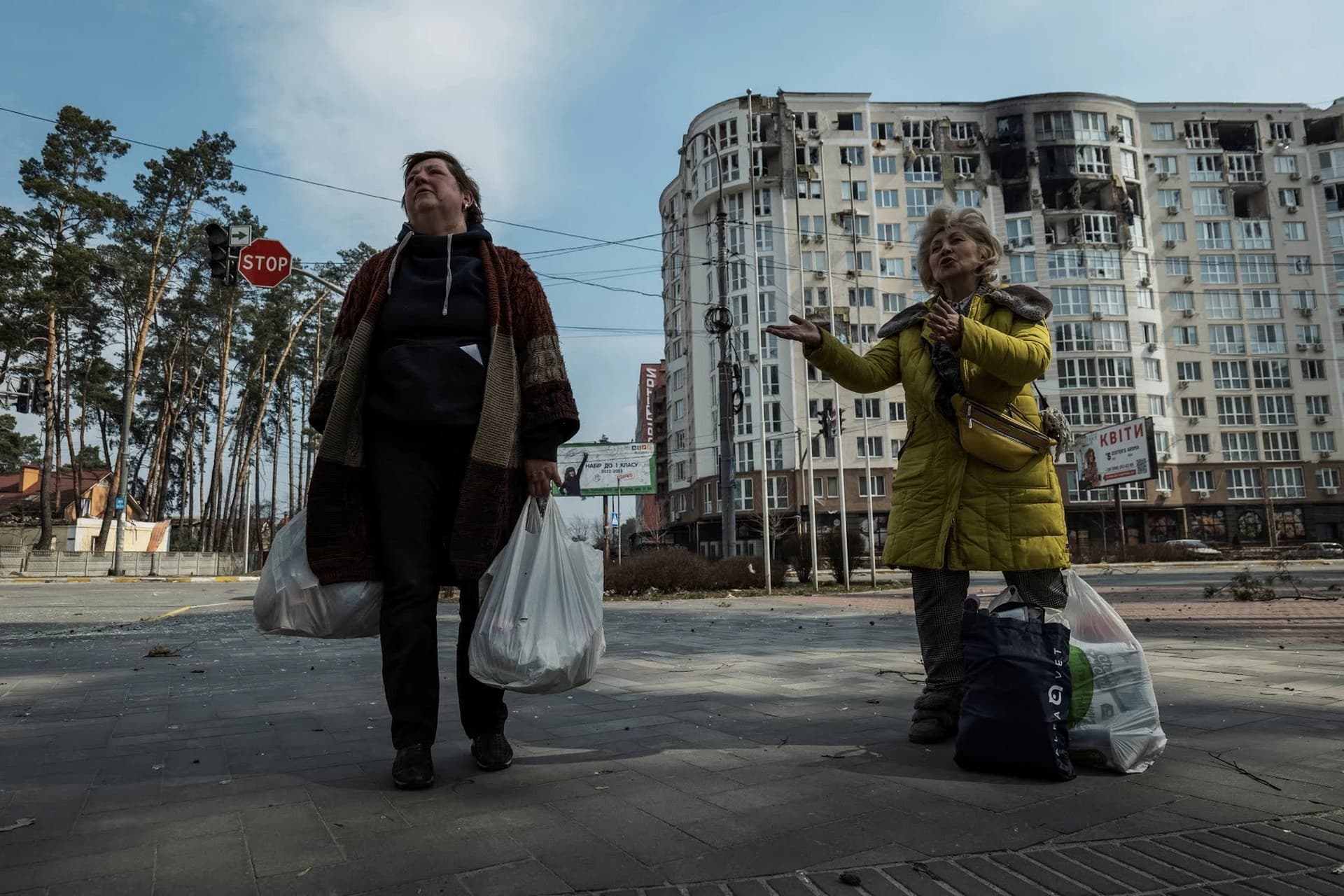 Local women carry food found at a supermarket in the town of Irpin