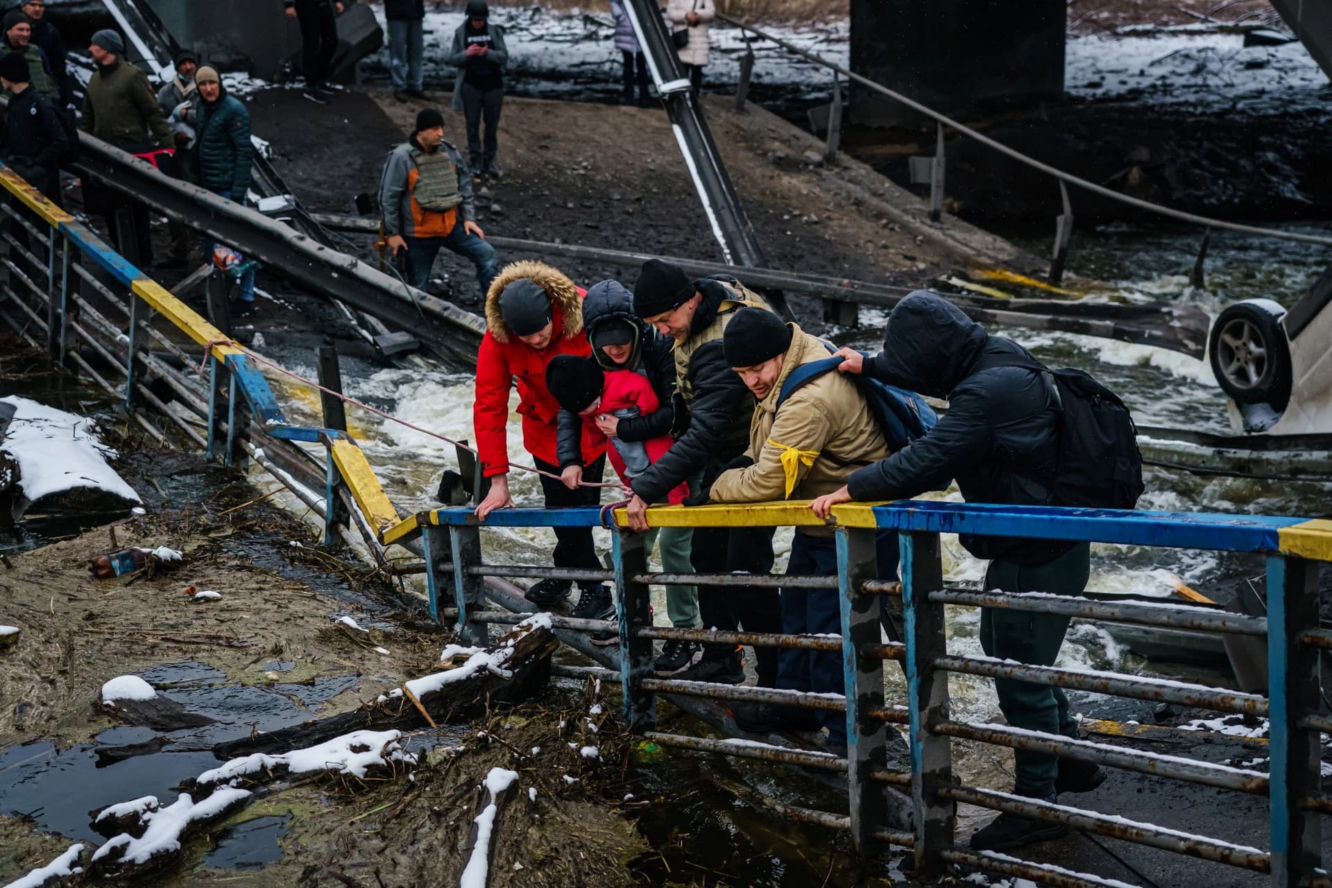 Soldiers help civilians cross a bridge in Irpin