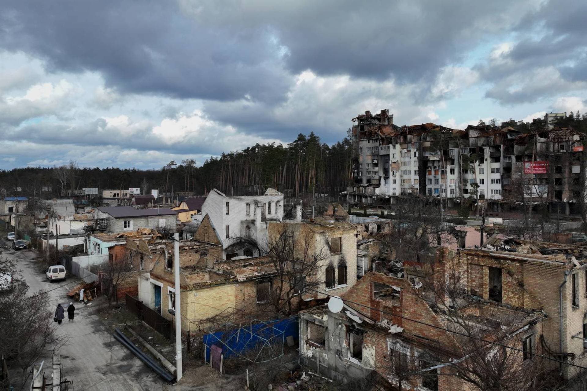 Women walk among destroyed buildings in Irpin