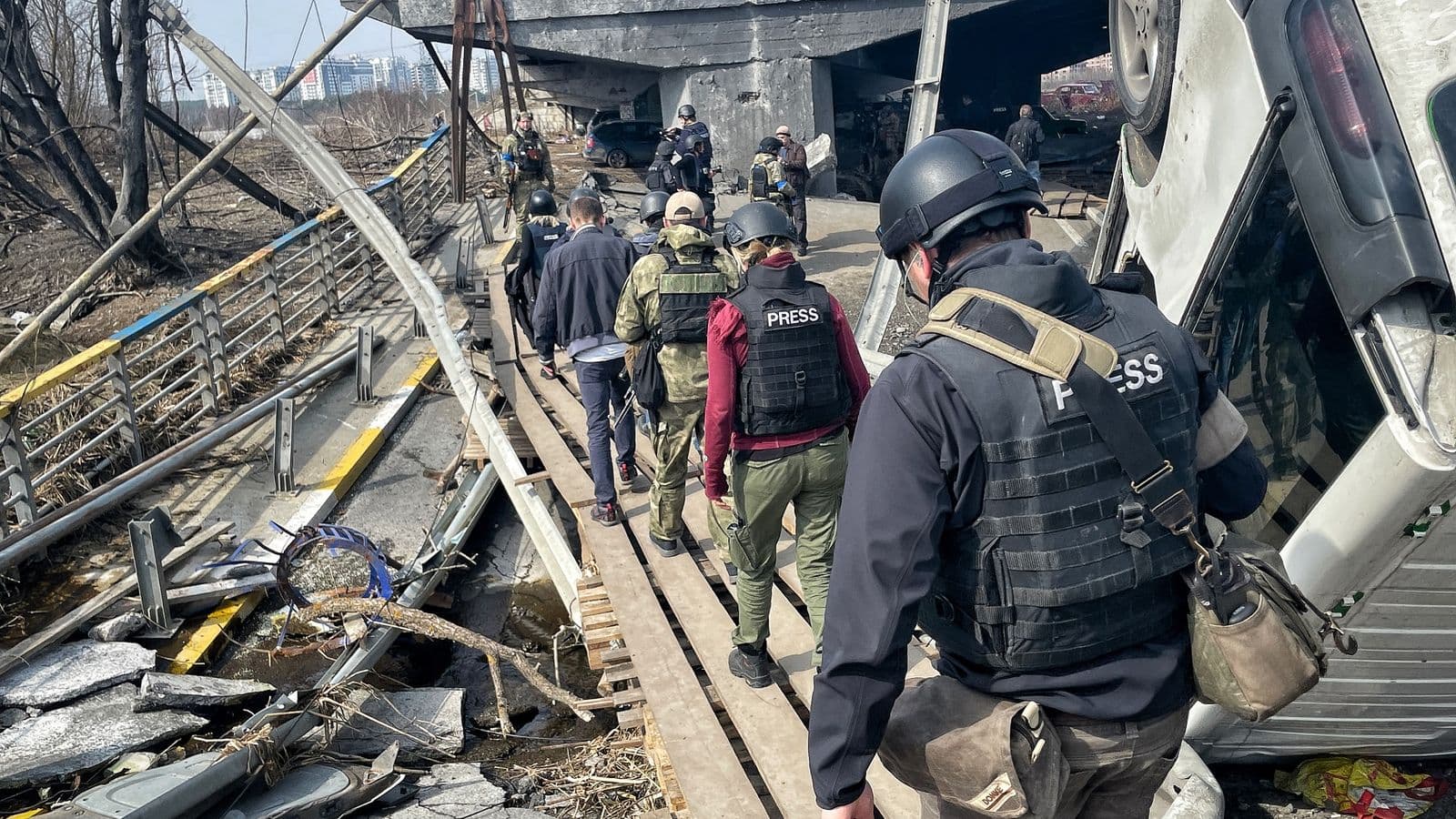 reporters walks near Irpin's bombed-out bridge