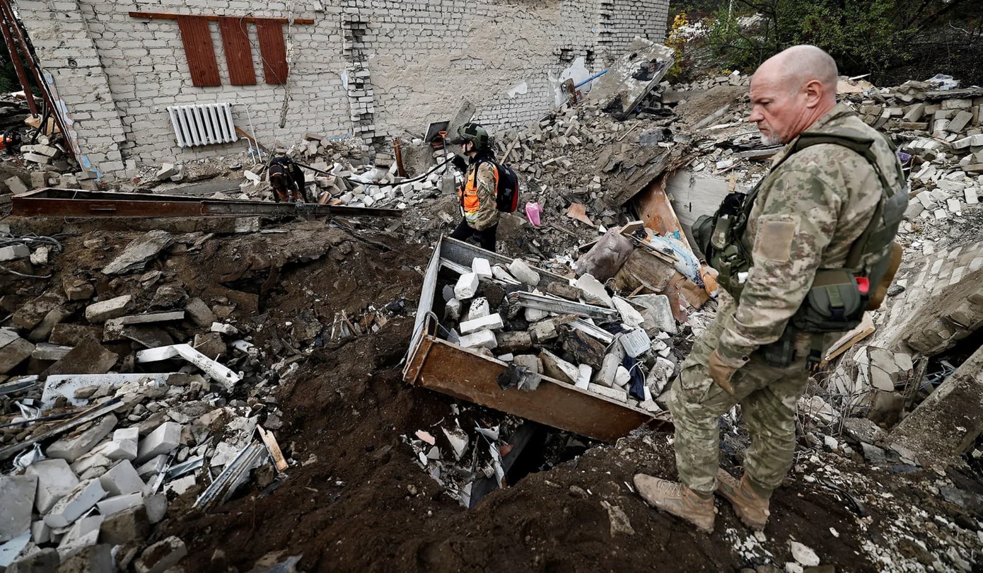 Firefighters and Ukrainian army soldiers search for bodies of people killed during a Russian attack among the remains of a building beside a TV tower in the recently liberated town of Izium