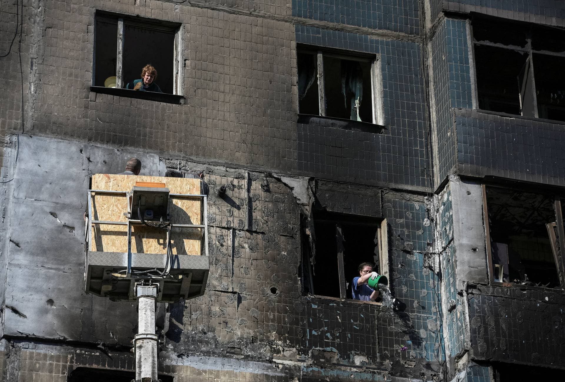 A woman speaks with workers covering broken windows in Kamyanske