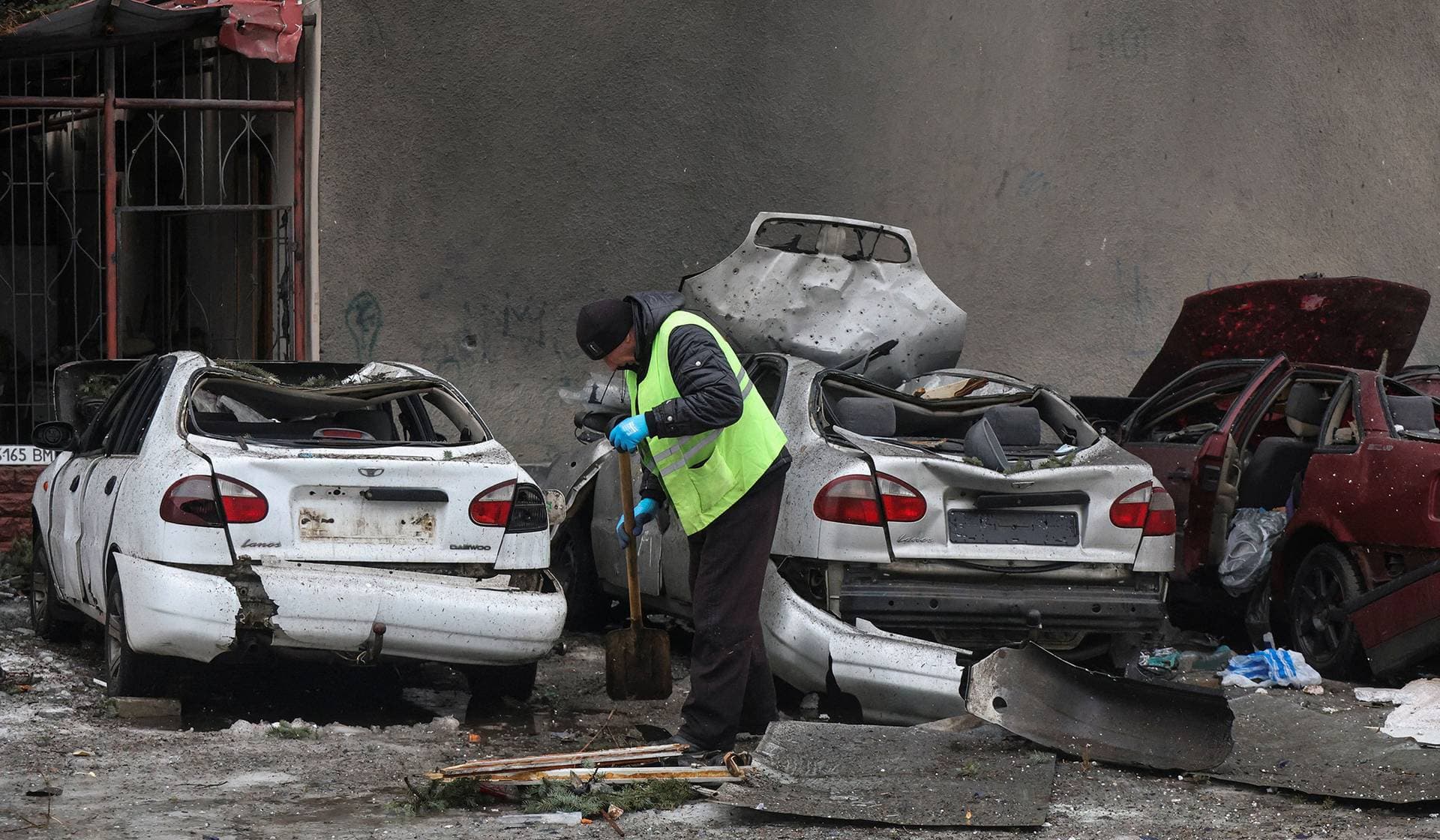 A municipal worker removes debris next to damaged cars outside an apartment building hit by a Russian drone strike in Kharkiv