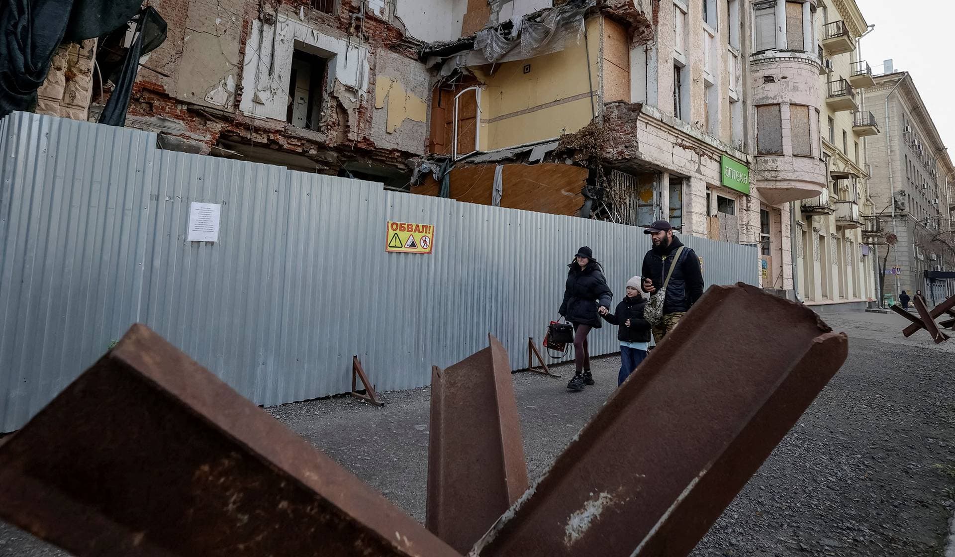 People walk next to a damaged building near anti-tank constructions in Kharkiv