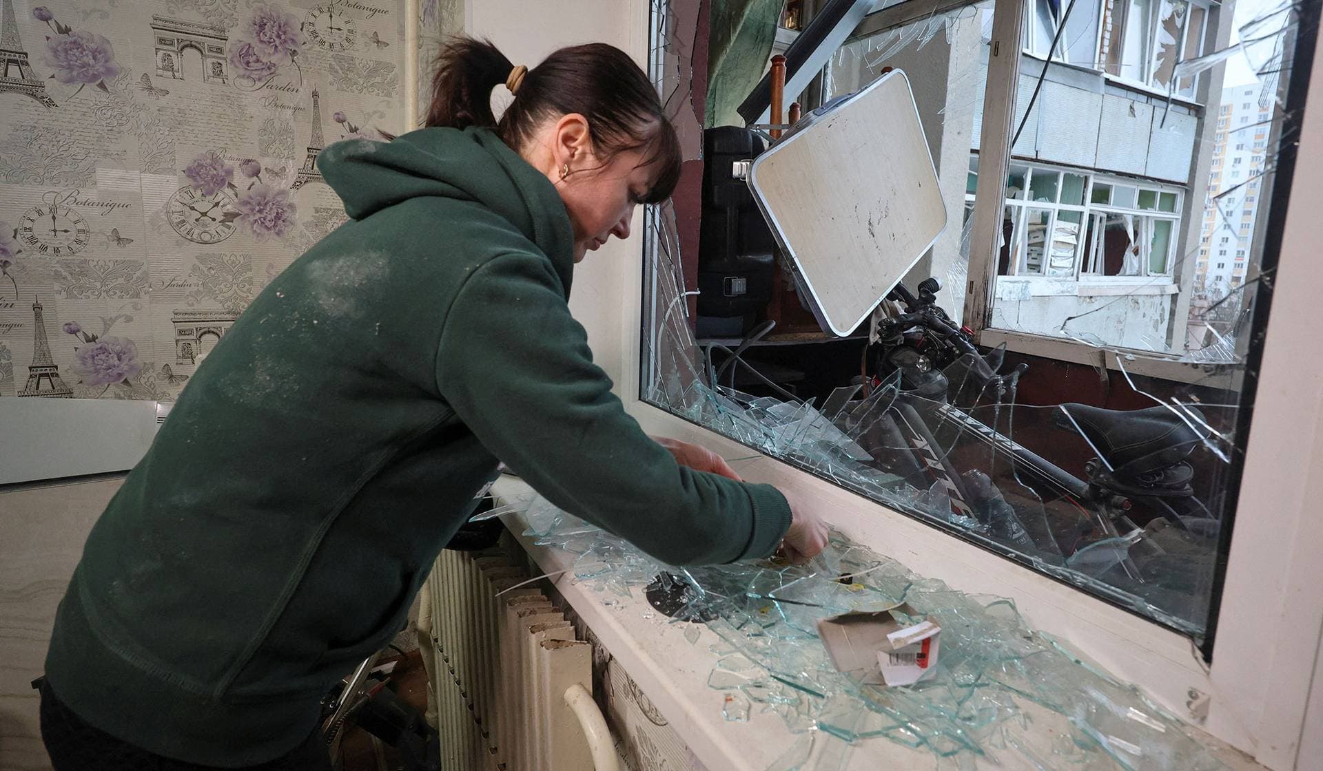A resident removes broken window glass inside her apartment damaged by a Russian drone strike in Kharkiv