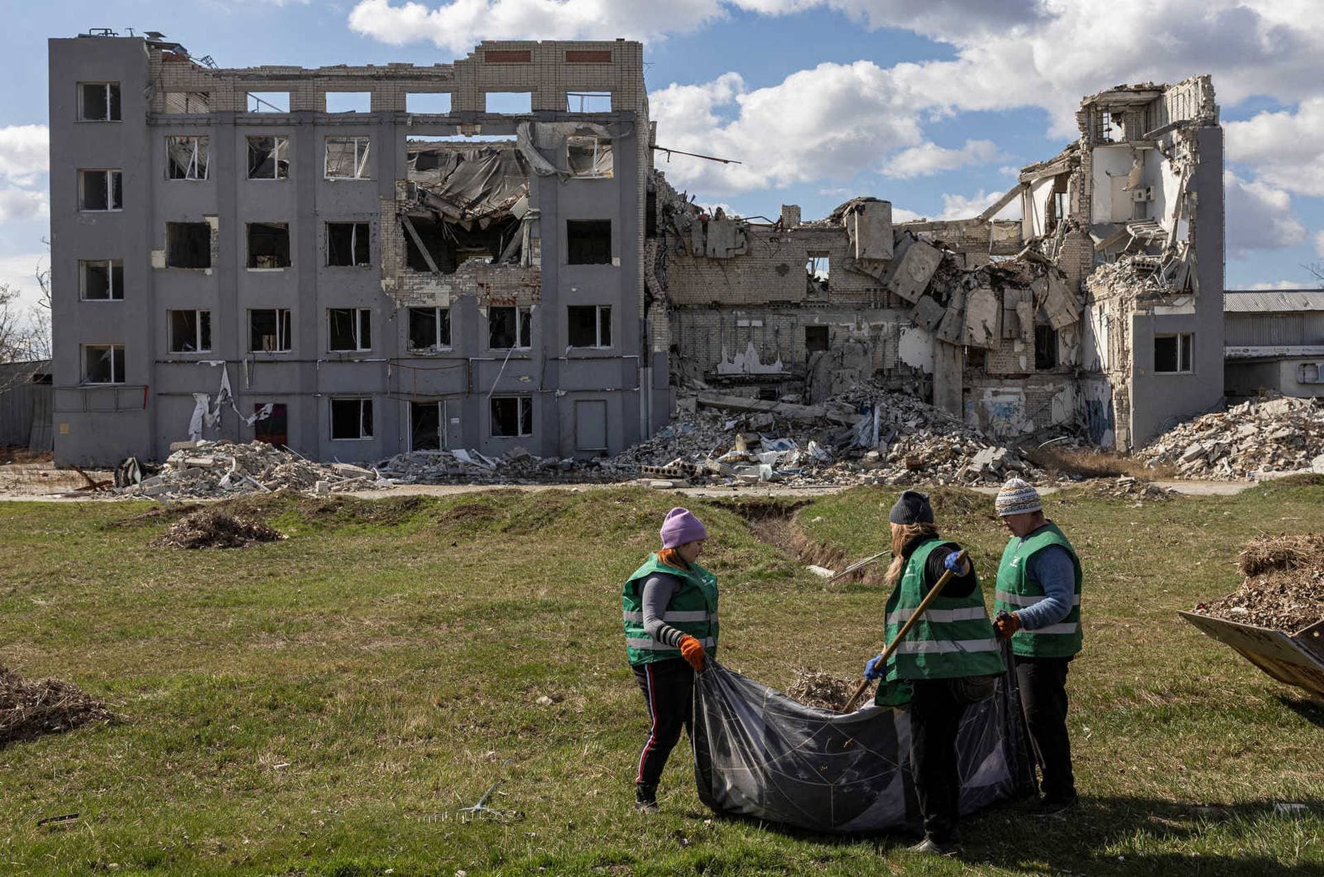 Municipal employees wearing armored jackets clean an area in front of a building heavily damaged in Kherson