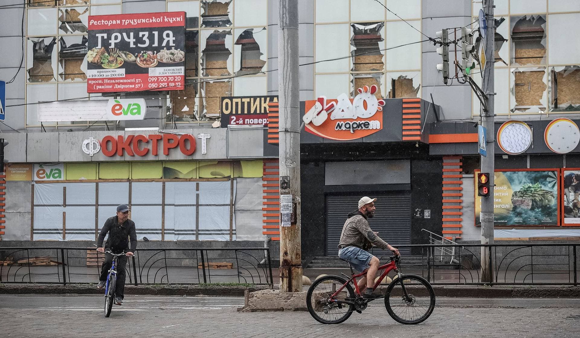 Men cycle past a damaged shopping mall in the frontline city of Kramatorsk