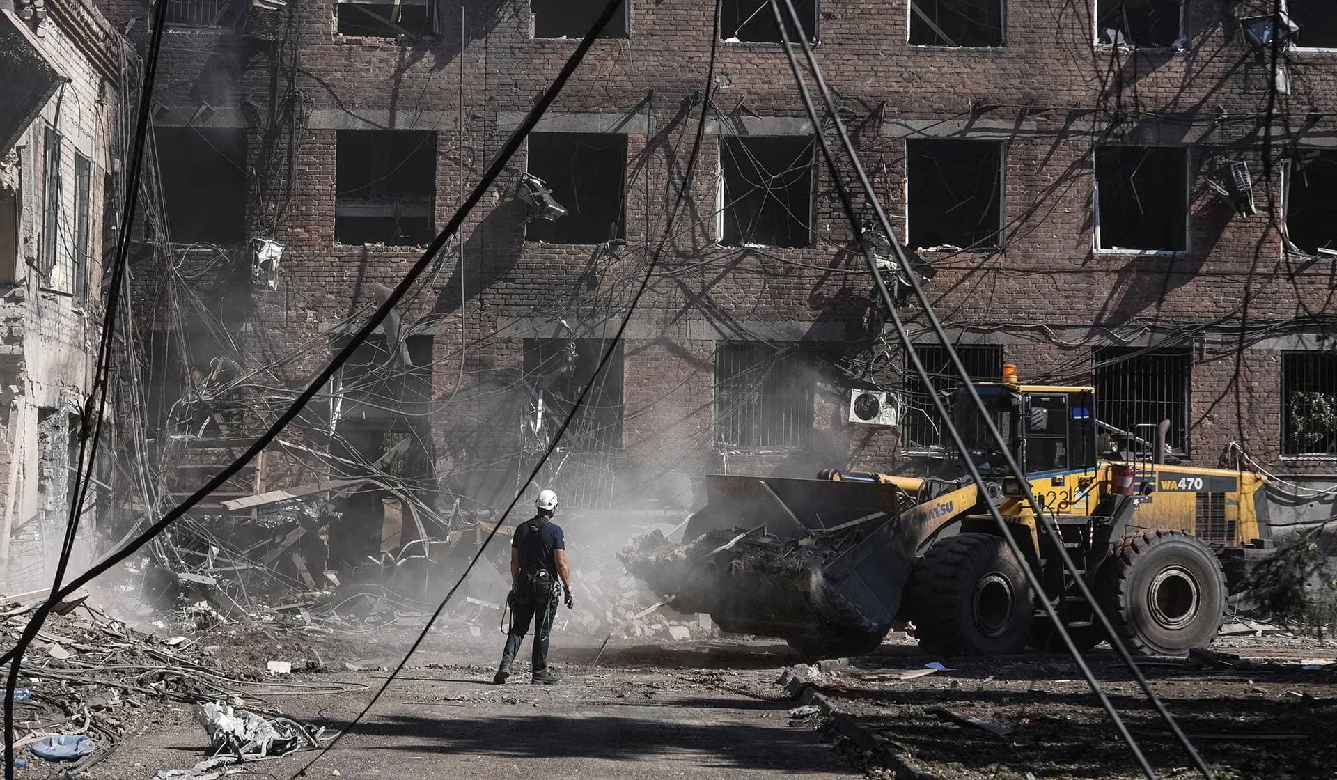 A man stands next to a vehicle as rescuers work at an apartment building hit by a Russian missile strike in Kryvyi Rih
