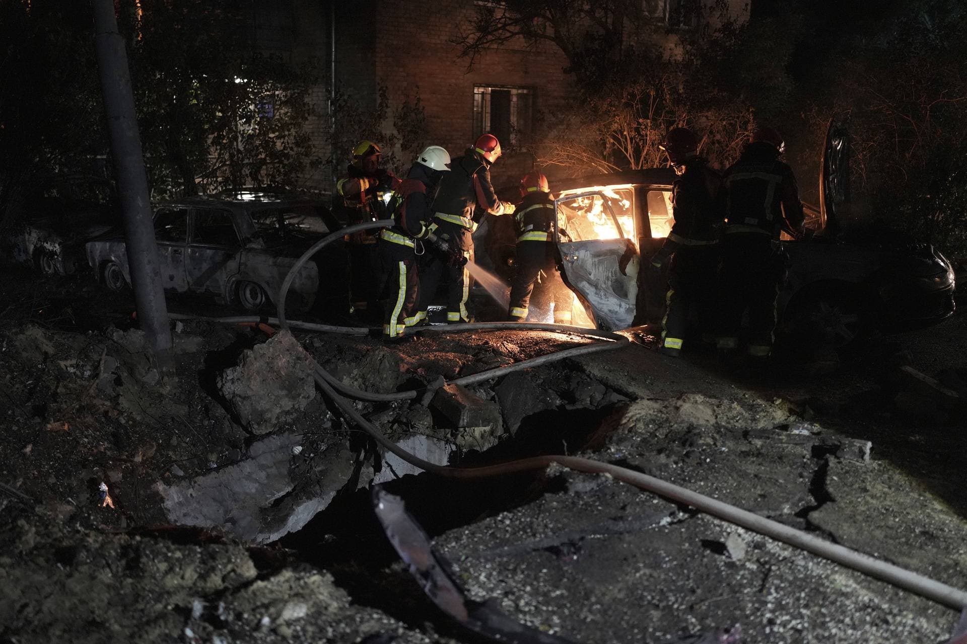 Emergency workers extinguish a fire in a parked car, caused by falling debris from the latest aerial Russian attack in Kyiv