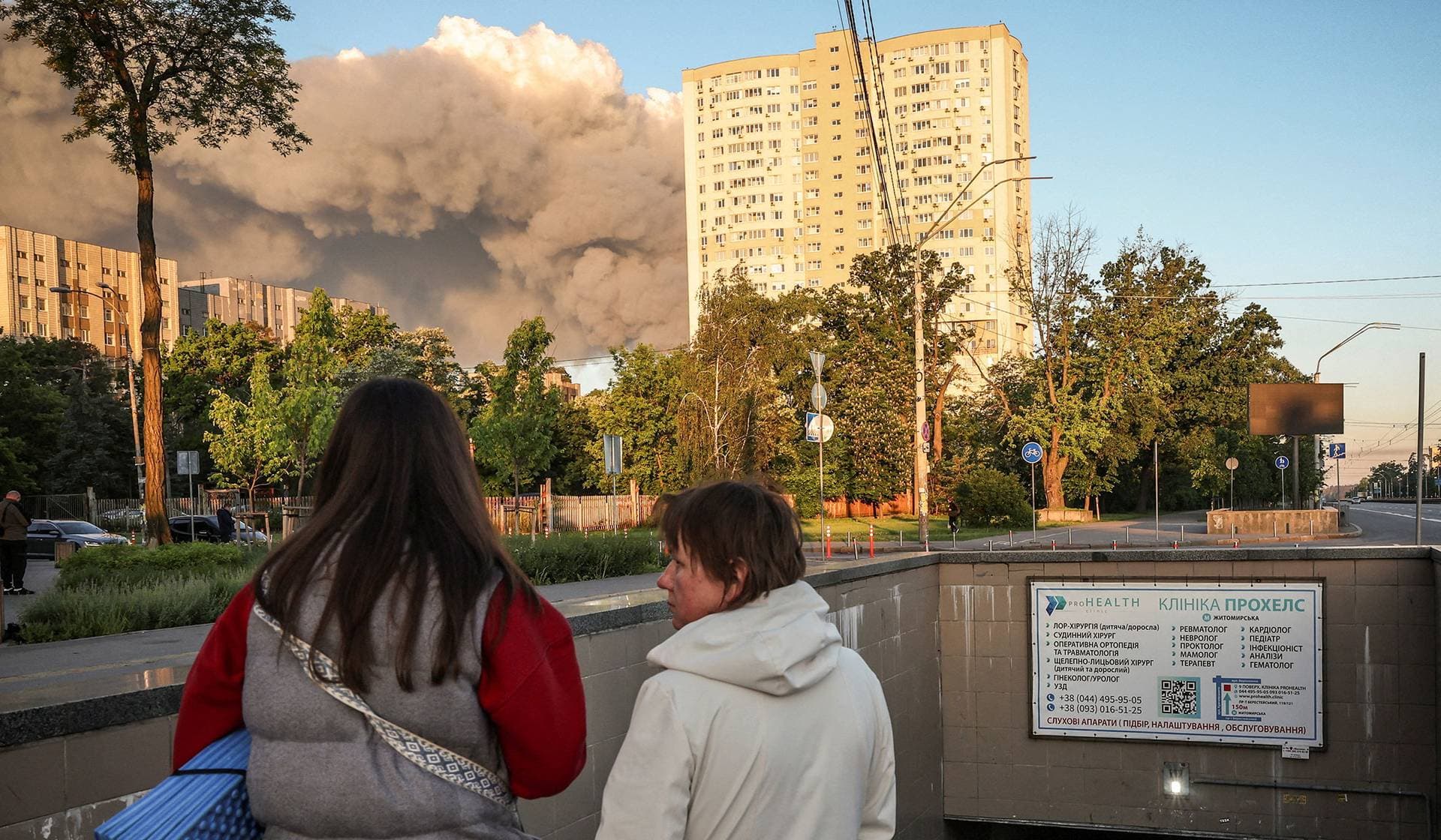People walk from a metro station where they took shelter during an overnight Russian missile and drone strike as smoke rises from the outskirts of Kyiv
