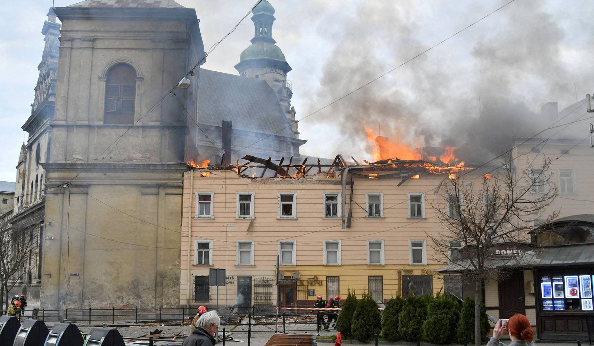 Residents look at firefighters who work at the site of a building hit by a Russian drone strike in downtown Lviv