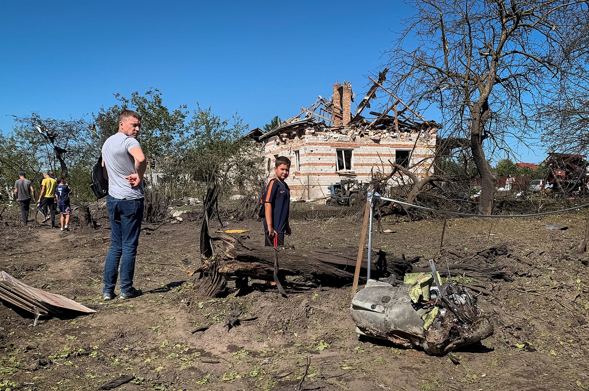 Local residents look at a part of a missile as they stand near residential buildings destroyed during a Russian military strike in the village of Stavchany