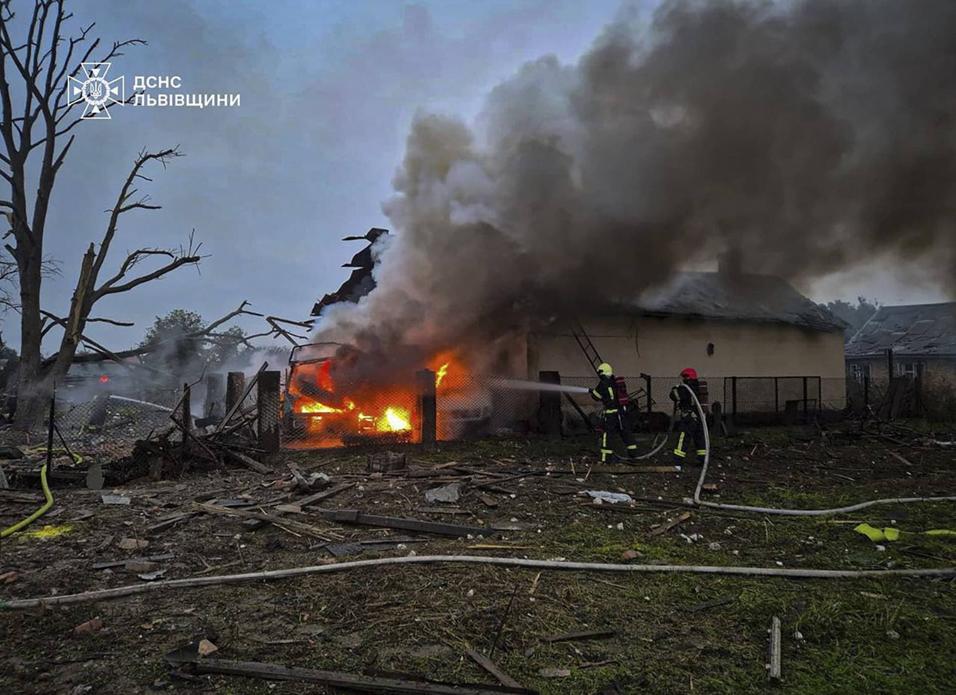 Firefighters extinguish a van on fire in a backyard of a residential house damaged during morning Russian drone and missile strikes in Lviv Region