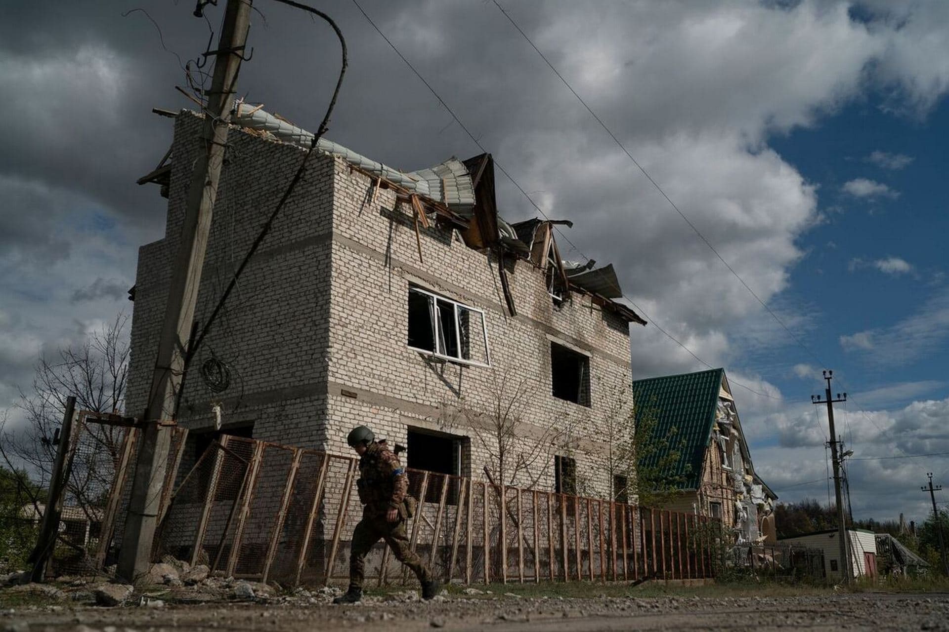 A Ukrainian serviceman walks past a damaged building in the retaken village of Shchurove