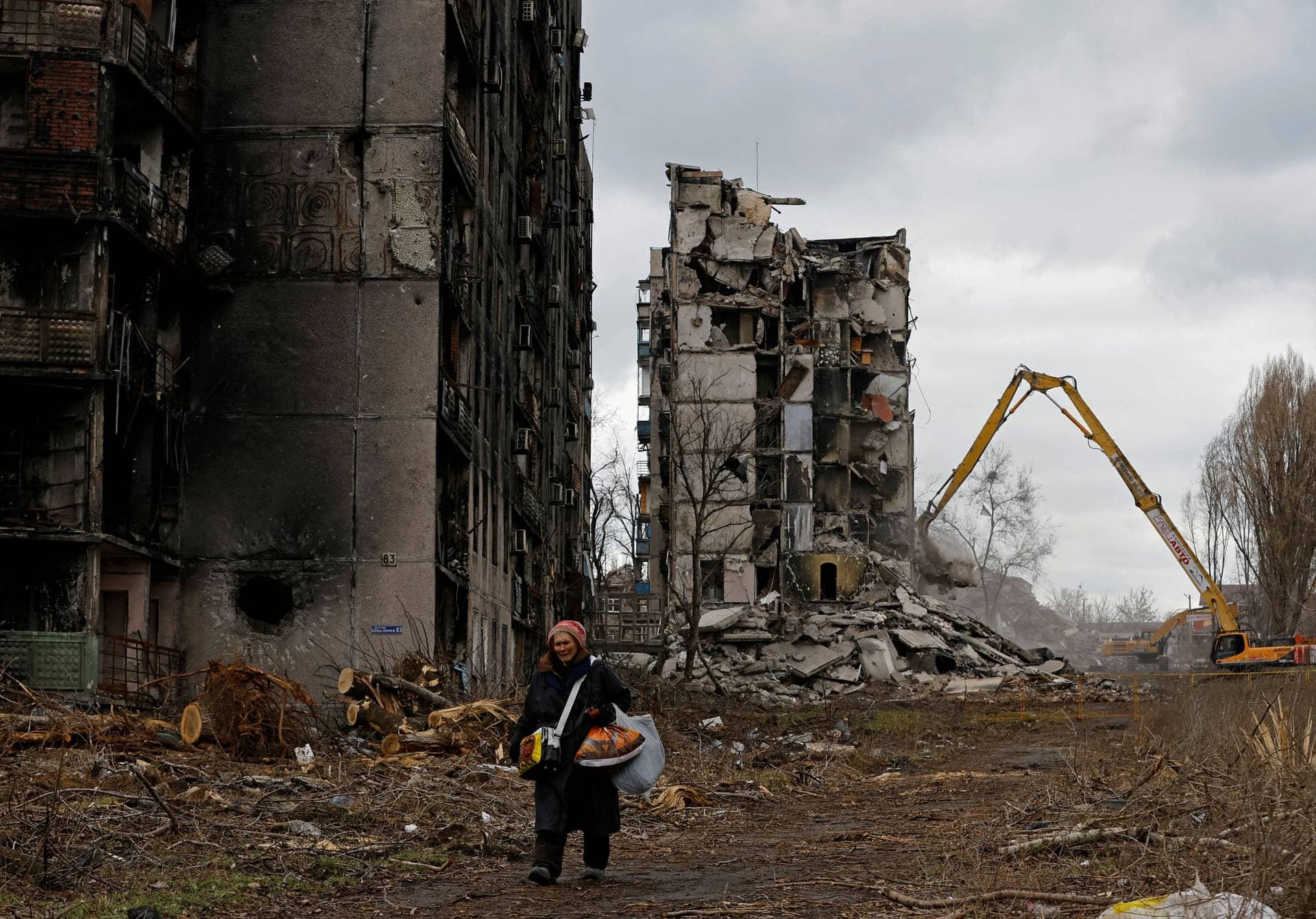 A woman reacts as she walks through her neighbourhood past destroyed apartment blocks in Mariupol