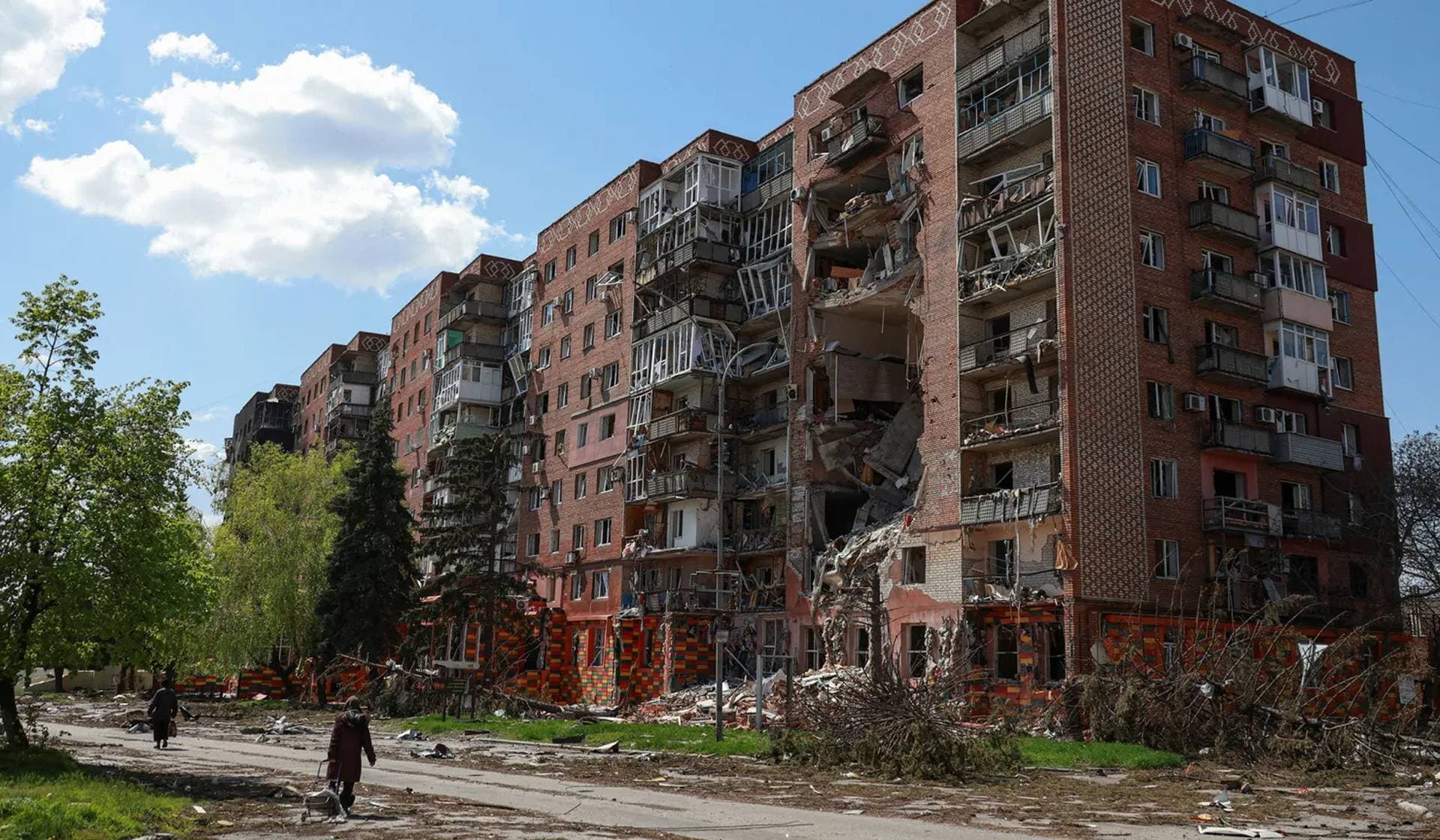 Residents walk next to an apartment building hit by Russian military strikes in the front line town of Pokrovsk