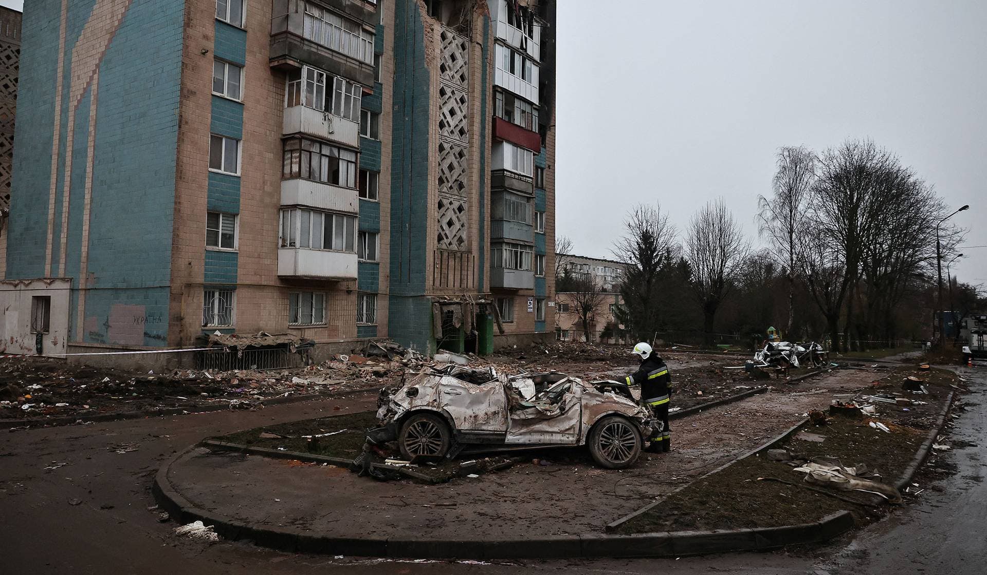 A firefighter looks at a car that was destroyed during a deadly Russian missile strike on an apartment building in Ternopil