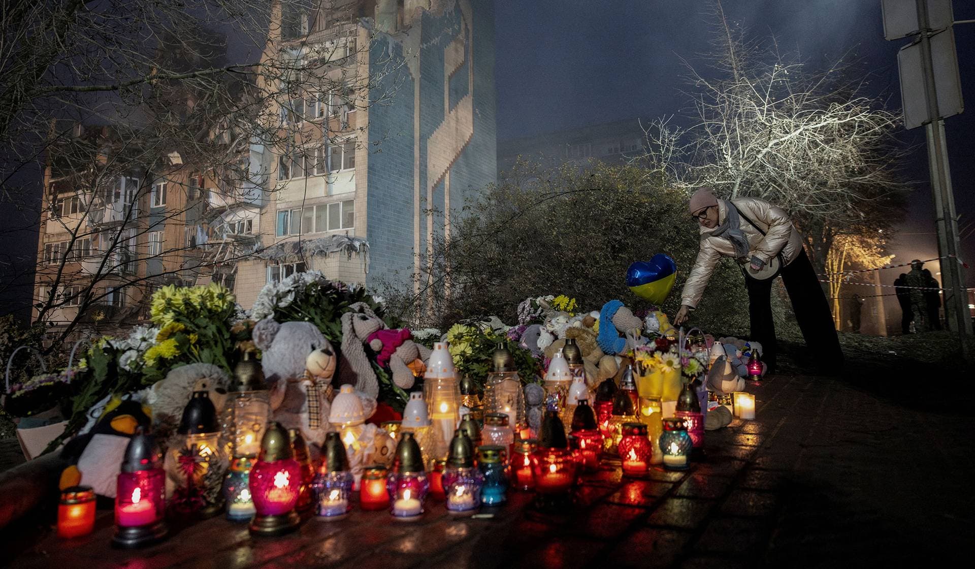 A woman places a candle at a makeshift memorial in front of an apartment building hit yesterday by a Russian missile in Ternopil