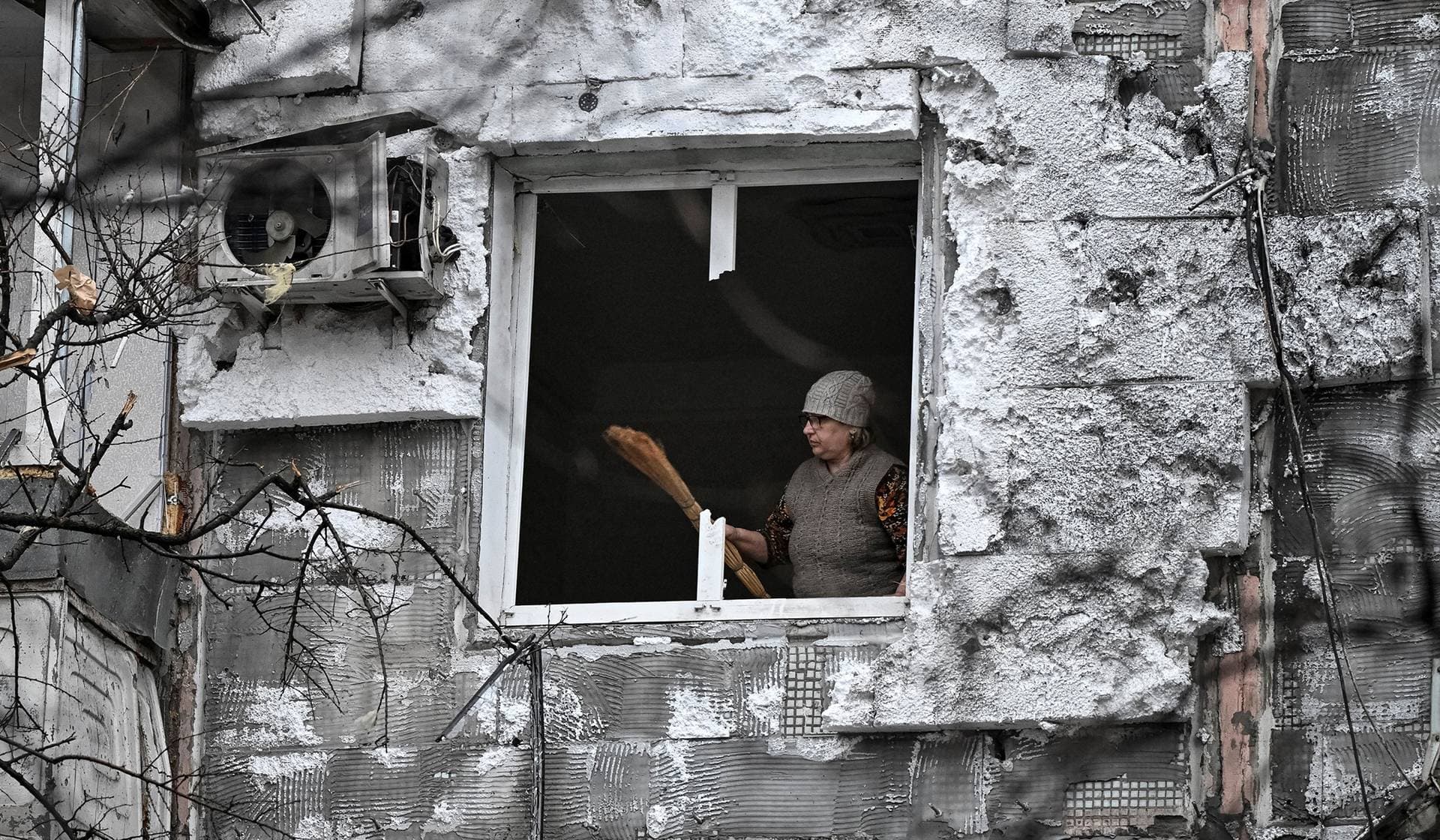 A woman removes broken glass from a window in her apartment hit by a Russian drone strike in Zaporizhzhia